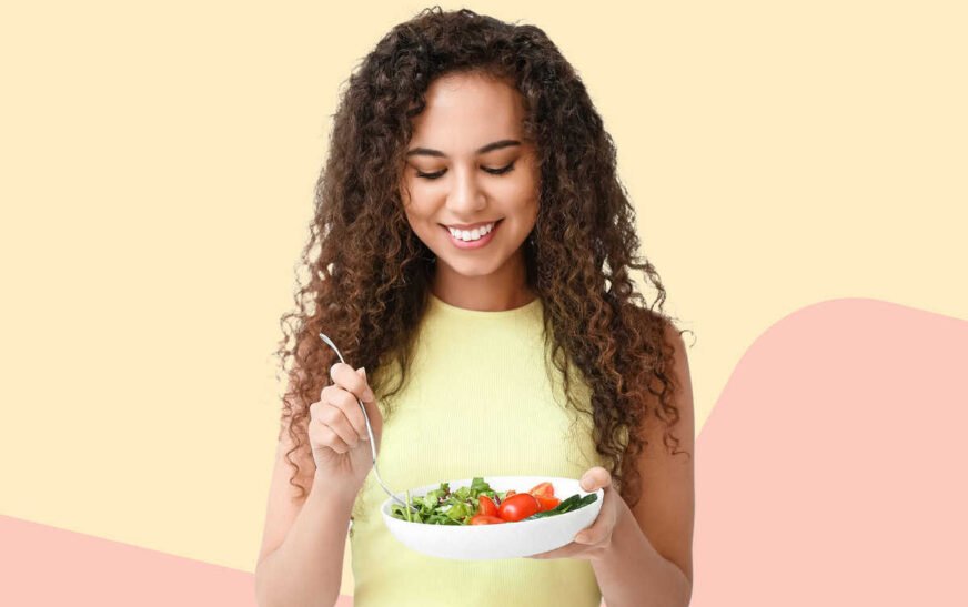 smiling-young-woman-with-curly-hair-eating-a-fresh-salad-bowl