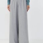 a-woman-in-light-gray-wide-leg-pleated-trousers-with-a-white-belt-and-a-teal-geometric-print-blouse