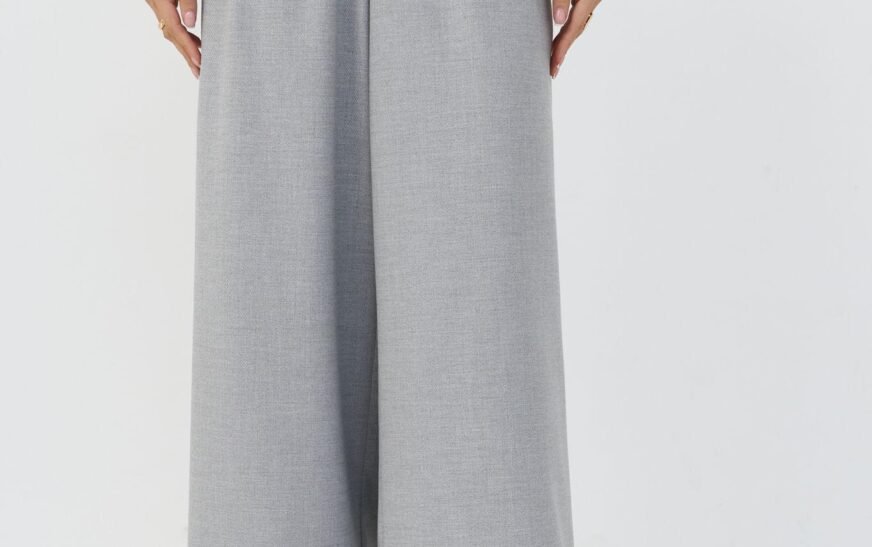 a-woman-in-light-gray-wide-leg-pleated-trousers-with-a-white-belt-and-a-teal-geometric-print-blouse
